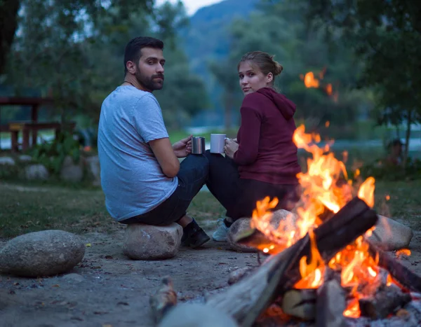 年轻夫妇坐在篝火旁 晚上拿着一杯茶或咖啡变暖自己 — 图库照片