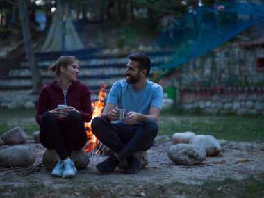 Bir bardak çay veya kahve kendilerini ısınma tutan akşam kamp ateşi etrafında oturan genç çift