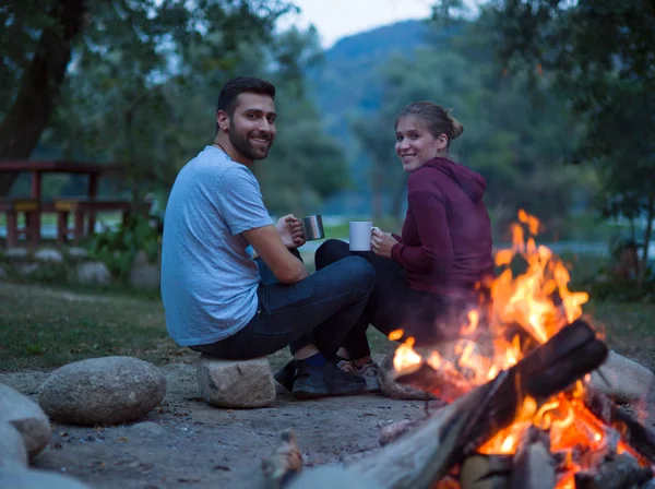 年轻夫妇坐在篝火旁 晚上拿着一杯茶或咖啡变暖自己 — 图库照片