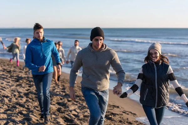 一群年轻的朋友在秋天的一天里一起在海滩上跑步 — 图库照片