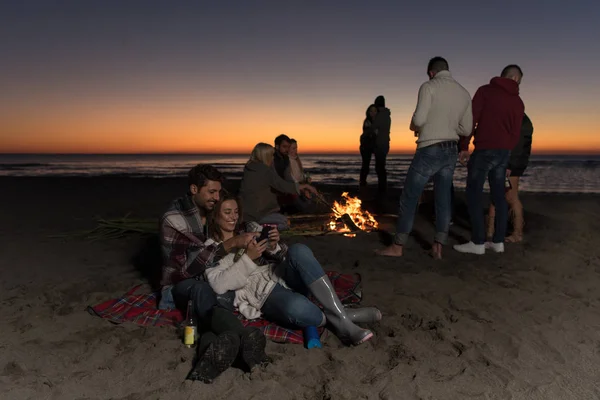 Пара Использующая Мобильный Телефон Время Осенней Пляжной Вечеринки Друзьями Пьющими — стоковое фото
