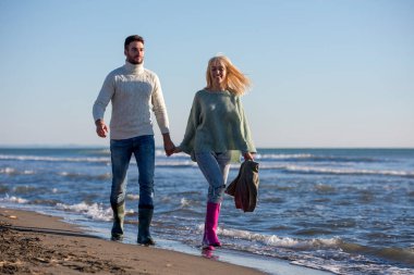 Genç çift, sonbahar güneşli bir günde kumsalda yürüyüp sarılıyor.