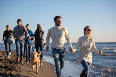 Bir grup genç arkadaş, güz günü boyunca kumsalda birlikte koşuyorlar.
