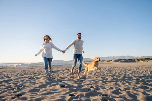 Pareja Corriendo Playa Sosteniendo Sus Manos Con Perro Día Autmun —  Fotos de Stock