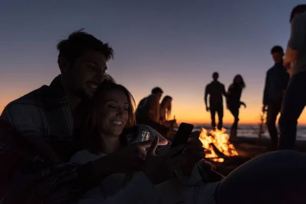 秋のビーチパーティーで携帯電話を使ってビールを飲みながら楽しむカップル — ストック写真
