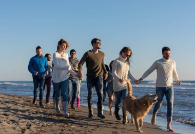 Bir grup genç arkadaş, güz günü boyunca kumsalda birlikte koşuyorlar.
