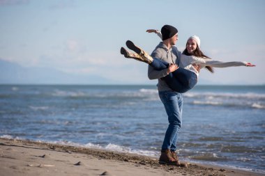 Genç çift, sonbahar güneşli bir günde kumsalda yürüyüp sarılıyor.