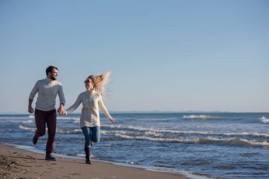 Genç çift, sonbahar güneşli bir günde kumsalda yürüyüp sarılıyor.