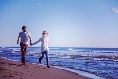 Genç çift, sonbahar güneşli bir günde kumsalda yürüyüp sarılıyor.