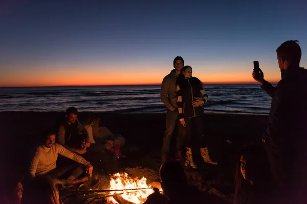 太陽が沈み始めるとビーチでたき火で楽しいビールを飲みながら幸せなケアフリー若い友人 — ストック写真