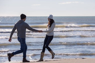 Genç çift, sonbahar güneşli bir günde kumsalda yürüyüp sarılıyor.