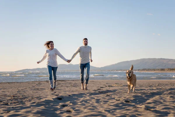 犬と手をつないでビーチを走るカップル秋の日 — ストック写真