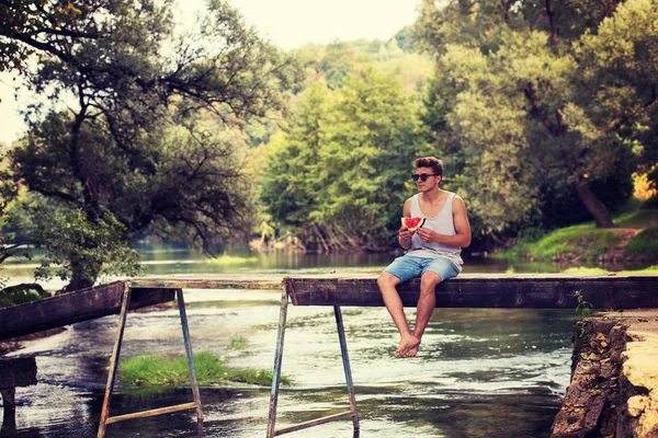 Junger Mann Genießt Wassermelone Während Auf Der Holzbrücke Über Den — Stockfoto