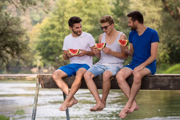 Gruppe Junger Männer Genießt Wassermelone Während Sie Auf Der Holzbrücke — Stockfoto