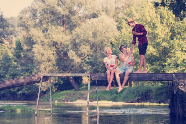 Jóvenes Amigos Disfrutando Sandía Mientras Sienta Puente Madera Sobre Río —  Fotos de Stock