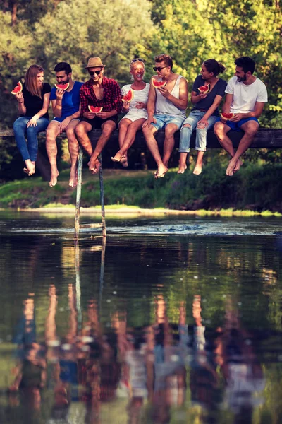 一群年轻的朋友享受西瓜 而坐在木桥过河在美丽的自然 — 图库照片