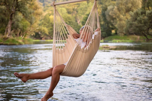 年轻的金发女子休息在吊床上享受大自然的河岸 — 图库照片