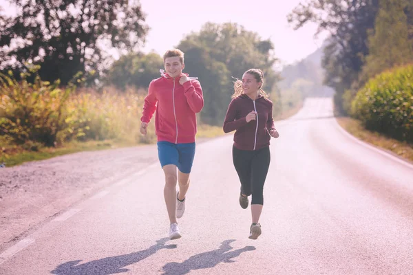 国の道路に沿ってジョギングしながら健康的なライフ スタイルを楽しむ若いカップル — ストック写真