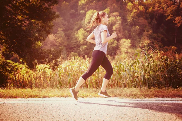 国の道路に沿ってジョギングしながら健康的なライフ スタイルを楽しんでいる若い成人女性ランナー — ストック写真