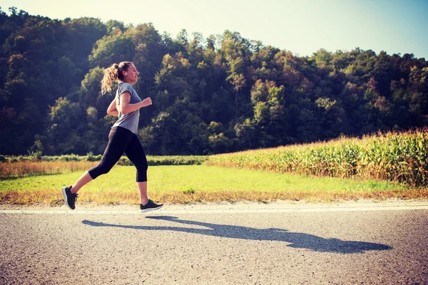 国の道路に沿ってジョギングしながら健康的なライフ スタイルを楽しんでいる若い成人女性ランナー — ストック写真