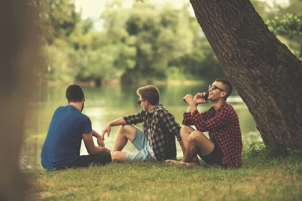 一群年轻男子享受自然坐在河岸上 — 图库照片