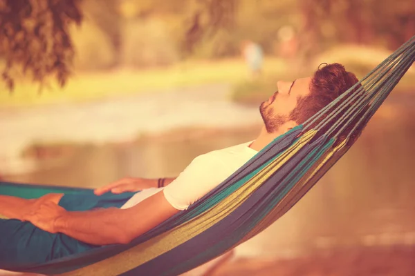 Genç Adam Nehir Kıyısında Doğanın Tadını Çıkarırken Hamakta Dinleniyor — Stok fotoğraf