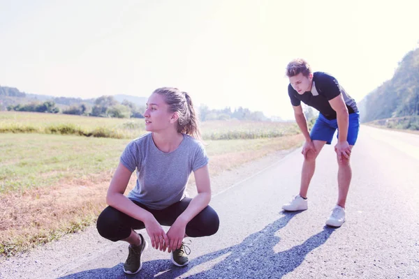 国の道路に沿ってジョギング中休んで若いカップル — ストック写真