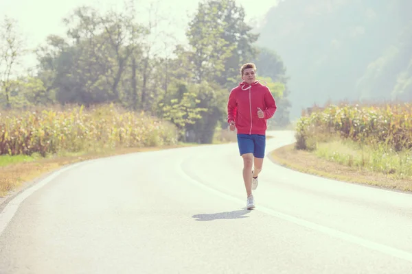 国の道路に沿ってジョギングしながら健康的なライフ スタイルを楽しんでいる若い男 — ストック写真