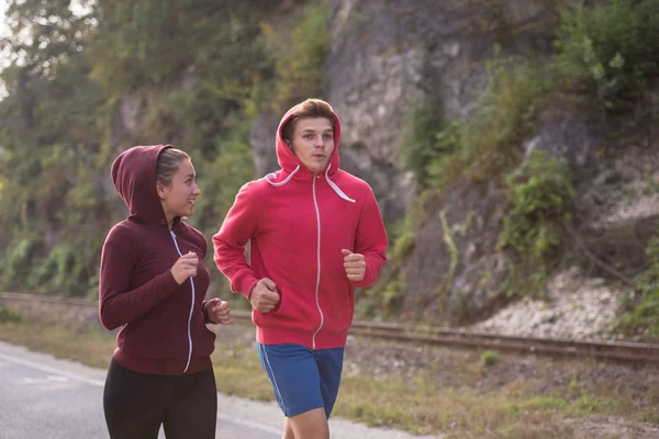 国の道路に沿ってジョギングしながら健康的なライフ スタイルを楽しむ若いカップル — ストック写真