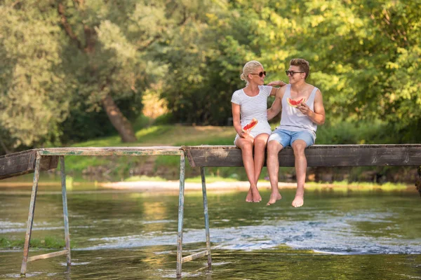 情侣在爱享受西瓜 而坐在木桥上的河在美丽的自然 — 图库照片