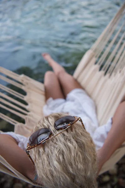 年轻的金发女子躺在吊床上 而享受自然在河岸上 — 图库照片