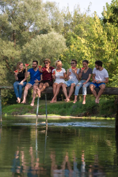 Grupo Jovens Amigos Desfrutando Melancia Enquanto Sentado Ponte Madeira Sobre — Fotografia de Stock