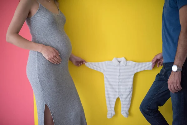 Güzel Bir Hamile Kadın Bebek Bodysuits Tutarak Renkli Arka Plan — Stok fotoğraf