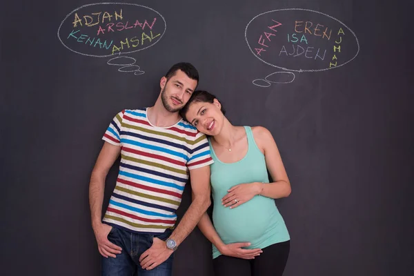 young pregnant couple thinking about names for their unborn baby and writing them on a black chalkboard