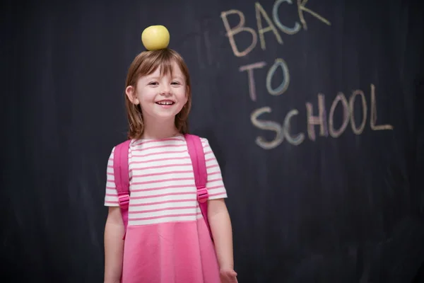 愉快的孩子抱着苹果在头上与回到学校绘画在黑板上的背景 — 图库照片