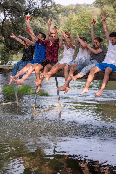 Grupo Jovens Amigos Desfrutando Melancia Enquanto Sentado Ponte Madeira Sobre — Fotografia de Stock