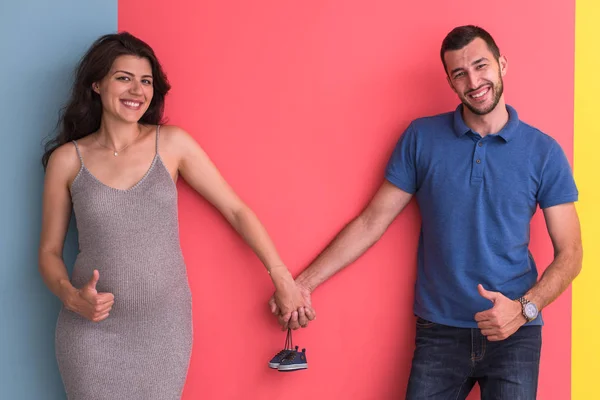 カラフルな背景 家族と親子関係の概念に分離された生まれたての赤ん坊靴を抱いた若い妊婦夫婦 — ストック写真