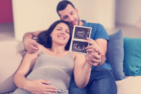 Mladí Těhotná Pár Hledá Ultrazvuk Foto Dítěte Při Odpočinku Pohovce — Stock fotografie