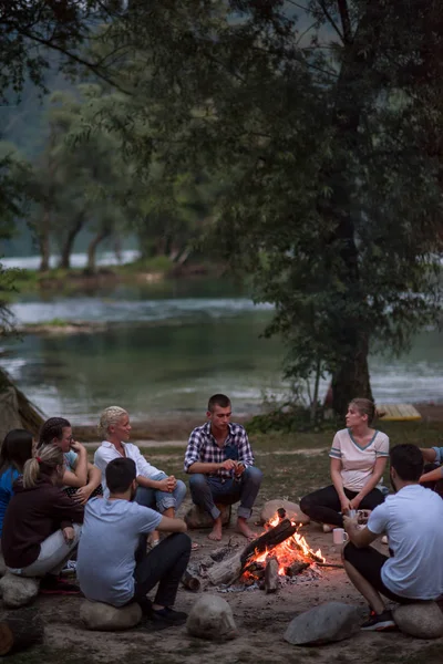 친구들이 강둑에서 모닥불 주위에서 저녁을 즐기면서 휴식을 취하고 — 스톡 사진
