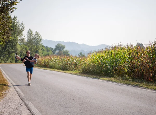 男人一边抱着一个女人一边沿着乡间小路慢跑 一边提出运动和健身的概念 — 图库照片