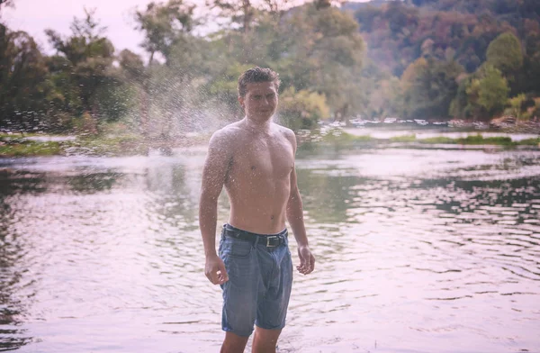 남자가 외투막 몸통을 가지고 강에서 일몰에 튀기며 재미있게 — 스톡 사진