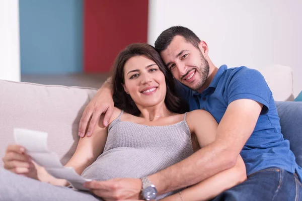 自宅のソファでリラックスしながら赤ちゃんの超音波写真を見て妊娠しているカップル — ストック写真