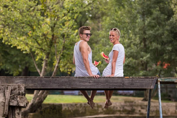 情侣在爱享受西瓜 而坐在木桥上的河在美丽的自然 — 图库照片