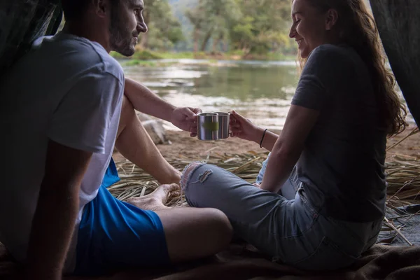 情侣在爱旅行和花时间在秸秆帐篷 而喝着热茶在河边 — 图库照片