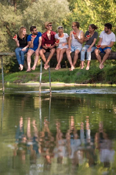 Grupo Jóvenes Amigos Disfrutando Sandía Mientras Están Sentados Puente Madera —  Fotos de Stock