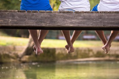 Grup ahşap köprü Nehri üzerinde asılı bacaklar odaklanarak oturan insan