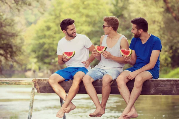 Gruppe Junger Männer Genießt Wassermelone Während Sie Auf Der Holzbrücke — Stockfoto