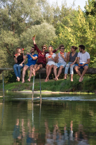 一群年轻的朋友享受西瓜 而坐在河上的木桥在美丽的自然 — 图库照片