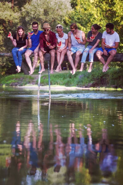 Grupo Jóvenes Amigos Disfrutando Sandía Mientras Están Sentados Puente Madera —  Fotos de Stock