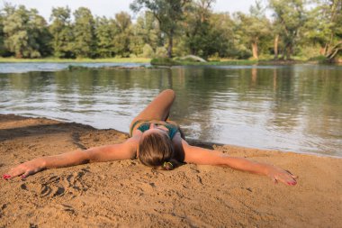Yeşil bikinili güzel seksi bir kız nehir kıyısında rahatlıyor ve eğleniyor.